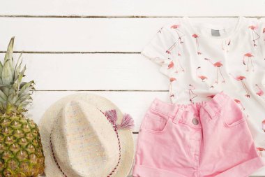Pembe kot şort ve gömlek, hasır şapka, ananas. Beyaz eski ahşap arka plan.