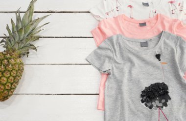 Üç tane gömlek, ananas, Pembe Flamingo yazdır. Beyaz eski ahşap arka plan.