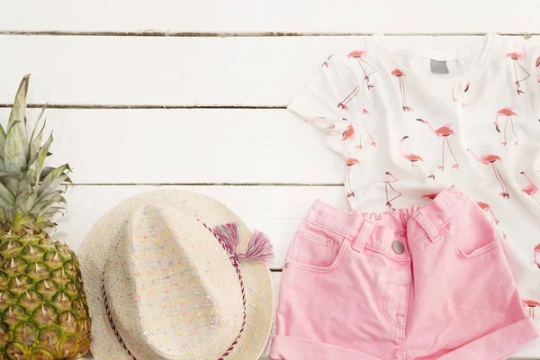 Pembe kot şort ve gömlek, hasır şapka, ananas. Beyaz eski ahşap arka plan.