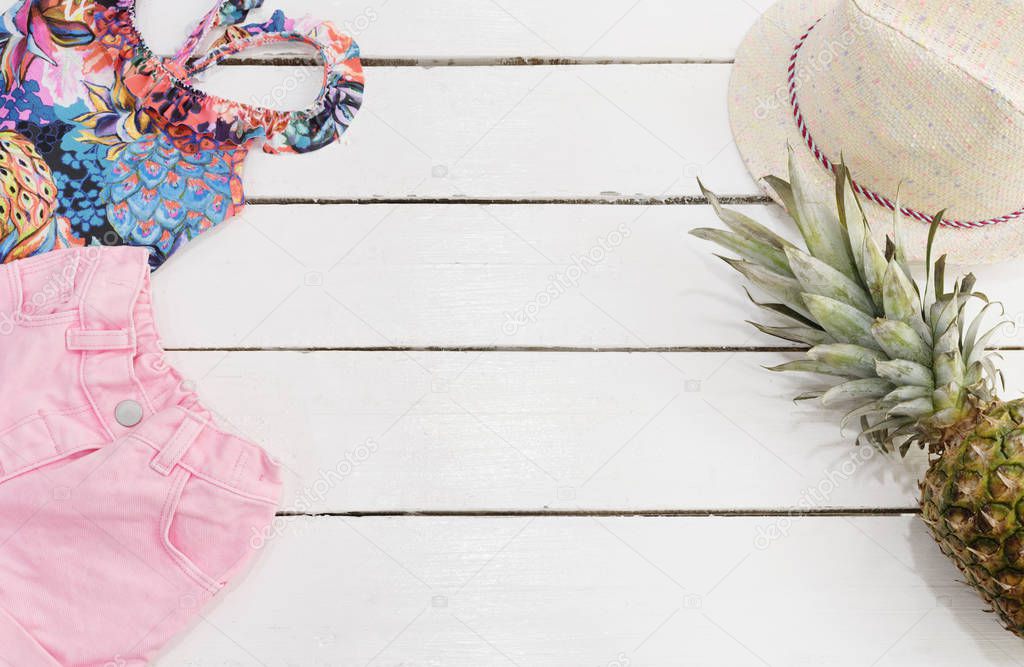Straw Hat, Tropical Print Swimsuit, Pink Jeans Shorts, Pineapple. White Old Wooden Background.