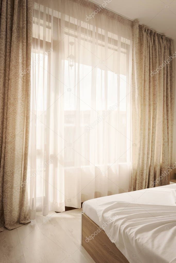 Hotel interior. Long beige curtains and tulle curtains, sheers on a window in the bedroom. Interior design concept.