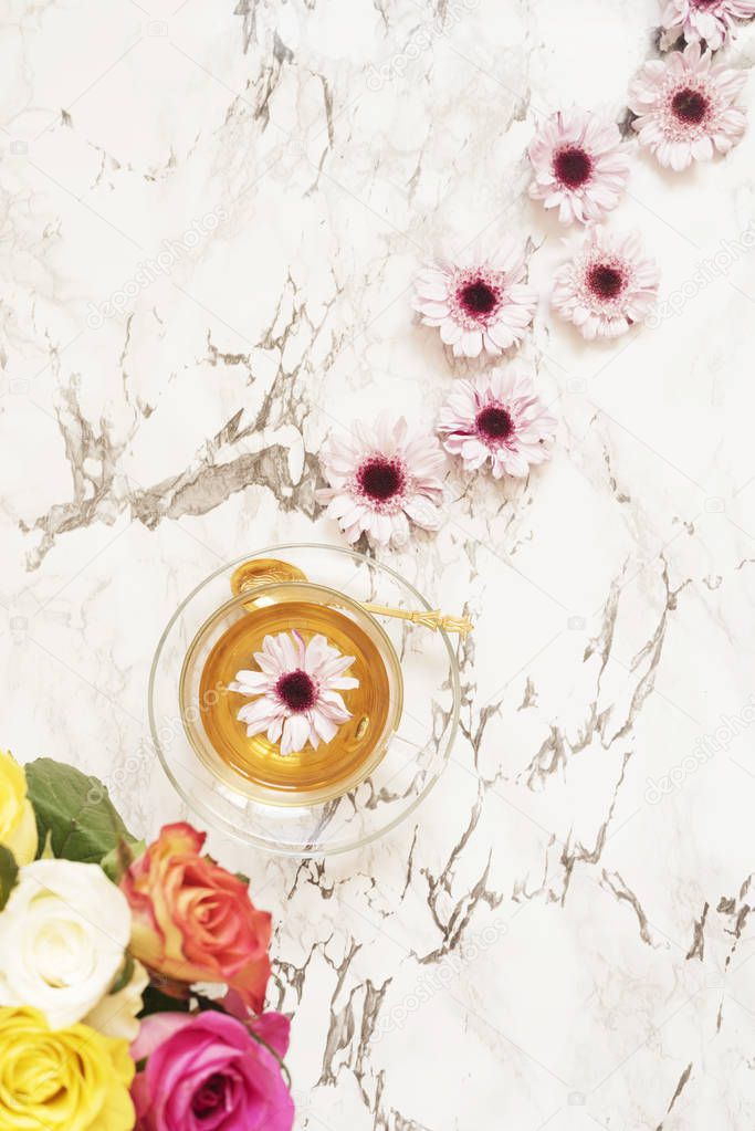 A cup of healthy herbal tea. Beautiful fresh flowers on light marble table, top view. Pink bouquet on a female work desk. Blogger lifestyle. Floral frame.