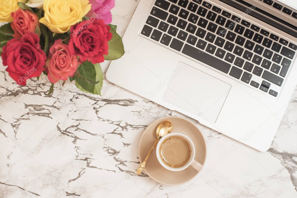 Feminine workplace concept. Freelance fashion comfortable femininity workspace in flat lay style with laptop, coffee cup, flowers on white marble background. Top view, bright, pink and gold.