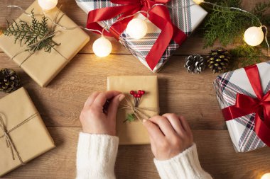 Bir kadının elleri kırsal arka planda klasik bir hediyeyle yayı bağlıyor. Kış tatilleri için şenlikli zemin: doğum günü, sevgililer günü, Noel, yeni yıl. Hediye paketleri hazırlayan bir kadın..