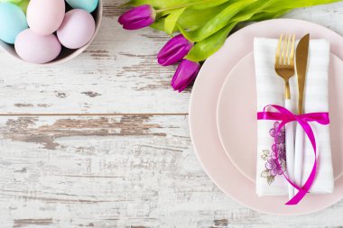 Paskalya Tablo ayarı, pastel renkli Paskalya yumurtaları, olay dekorasyon ile flatlay. Pembe yemekleri ve altın çatal ve kaşıkla hafif bir rustik ahşap arka plan üzerinde. Güzel mor bahar Lale çiçek