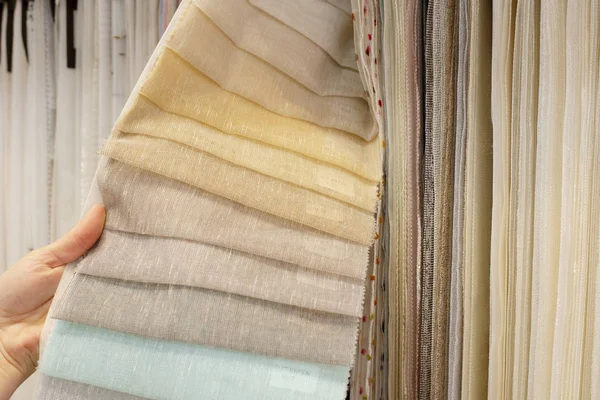 Young woman choosing fabric for new curtains in shop