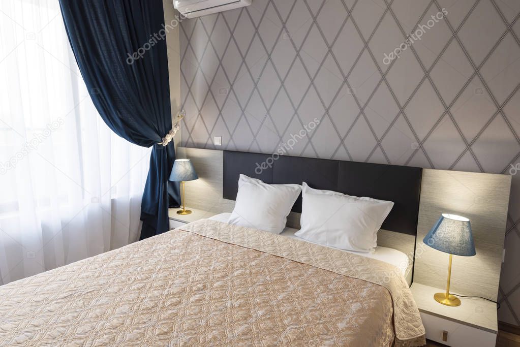 Interior of modern bedroom with cozy double bed. Windows with long curtains, drapery and sheers. Interior photography
