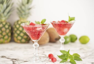 Buz ve ahududu ile iki ferahlatıcı kırmızı yarı saydam içecekler. Ahududu suyu yeşil bir yaprak ile süslenmiş, ve buz parçaları ve ahududu içecekler etrafında dağınık vardır