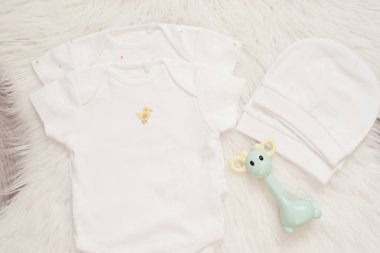 Bebek Maket. Bodysuits, Beyaz Şapka ve Çıngırak Oyuncak. Bebek Tulumları, Beyaz Kürklü Halıda Rompers. Yenidoğan Kavramı. Erkek veya Kız Unisex Giyim