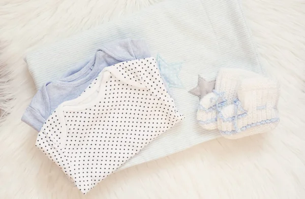 Manta azul, trajes de cuerpo, botas de bebé de punto y juguete de conejito en una alfombra de piel blanca. Mockup bebé. Concepto para recién nacidos. Bebé chico ducha invitación Imagen De Stock