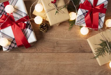 Noel geçmişi. Noel Kutuları ve Işıklar Üst Görünümü Zanaat ve Kırmızı Çizgili Kağıt Dal, Keten Kordon, Ahşap Masa Üzerinde Kırmızı Yay ile Süslenmiş