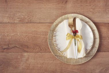 Noel tatil akşam yemeği yer ayarı - tabaklar, peçete, çatal, meşe masa arka plan üzerinde altın bauble süslemeleri. Altın tabaklarda çatal ve kaşık. Düz yatıyordu
