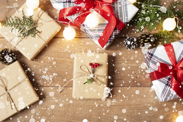 Fundo de Natal. Vista superior de caixas de Natal e luzes em artesanato e papel listrado vermelho decorado com filial, cabo de linho, arco vermelho na mesa de madeira. Neve desenhada — Fotografia de Stock