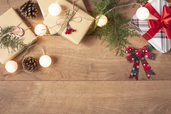 Fundo de Natal. Vista superior de caixas de Natal e luzes em artesanato e papel listrado vermelho decorado com filial, cabo de linho, arco vermelho na mesa de madeira. Espaço de cópia — Fotografia de Stock