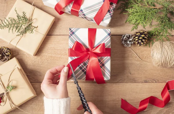 Fondo de Navidad. Manos femeninas cortando un arco rojo. Mujer Embalaje regalos de Navidad. Fondo de vacaciones. Vista superior, disposición plana, regalo de Adviento Fotos De Stock Sin Royalties Gratis