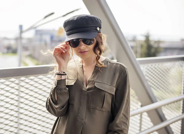 Retrato de modelo femenina de moda vestida casual en un lugar gruñón. Blogger de moda con camisa militar y sombrero en un puente peatonal Imagen De Stock