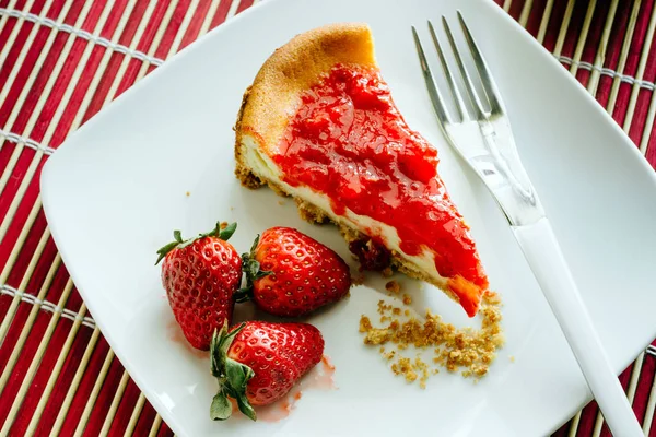 slice of homemade cheesecake with strawberry jelly served with fresh strawberries on white plate