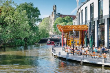 Amsterdam, Hollanda-13 Mayıs 2019: denizde bir tekne ile bir Kanal Görünümü, güneşli bir günde masalarda oturan insanlarla Bar Terası