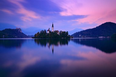 Alacakaranlık akşam Bled, Slovenya, ışık. Göl Adası, St Martin Katolik Kilisesi ve kale Sıradağları, Slovenya, Avrupa ile. Sonbahar manzarası göl kenarında. Ön planda yeşil ağaç yaprak.