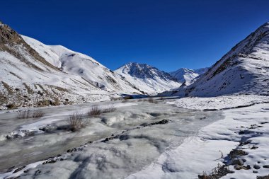 Rumbak Vadisi ve Yarutse yolu, Hemis NP, Ladak, Hindistan. Kış boyunca karlı nehir, Himalayalar. Hindistan 'daki dağ manzarası vahşi doğa. Vadide karlı güneşli bir gün, bulutlu mavi bir gökyüzü.
