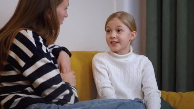 Sevgi dolu anne ve kız samimi bir anı paylaşıyor, sarı koltukta rahatça otururken derin bir sohbete dalıyor, gerçek duygularını ve aile dinamiği içinde anlayış gösteriyor.