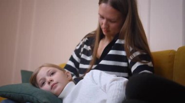 Kızını nazikçe destekleyen şefkatli bir anne yürekten tavsiyeler veriyor ve sıcak aile ortamında yumuşak sarı kanepede güvenli bir duygusal alan yaratıyor.