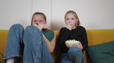 Anne ve kızı rahat sarı bir koltukta oturmuş, büyüleyici bir film izlerken bir kase patlamış mısırlarını paylaşıyor, sıcak ve iç açıcı bir aile anı yaratıyorlar.