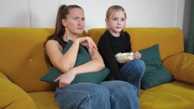 Anne ve kızı rahat sarı bir koltukta oturmuş, büyüleyici bir film izlerken bir kase patlamış mısırlarını paylaşıyor, sıcak ve iç açıcı bir aile anı yaratıyorlar.