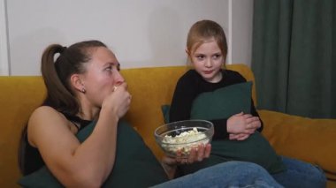 Anne ve kızı, rahat bir koltukta oturup, cam kaseden patlamış mısır yerken ve korkmuş ifadeler sergilerken TV 'de bir korku filmi izliyorlar.