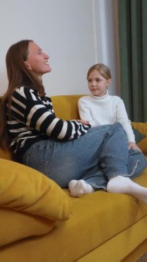 Anne küçük kızını dikkatle dinliyor, bir şeyi açıklıyor, oturma odasındaki rahat bir koltukta birlikte oturuyor, ciddi bir konuşma videosu var.