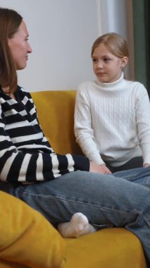 Anne küçük kızını dikkatle dinliyor, bir şeyi açıklıyor, oturma odasındaki rahat bir koltukta birlikte oturuyor, ciddi bir konuşma videosu var.