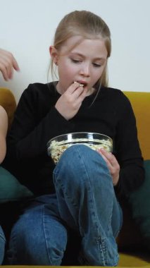 Anne ve kızı, rahat bir koltukta oturup, cam bir kaseden patlamış mısır yerken ve korkmuş yüz ifadelerini dikey olarak gösterirken televizyonda korku filmi izliyorlar.