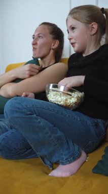 Anne ve kızı, rahat bir koltukta oturup, cam bir kaseden patlamış mısır yerken ve korkmuş yüz ifadelerini dikey olarak gösterirken televizyonda korku filmi izliyorlar.