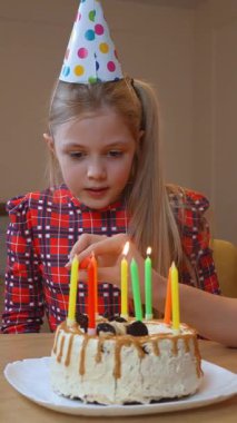 Doğum günü kızı şenlikli parti şapkası takıyor, pastaya renkli mumlar yakıyor, annesinin nazik yardımıyla, çocukluk günlerinin sıcak aile kutlamalarını dikey videolarını yakıyor.
