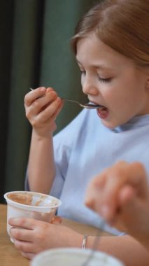 Anne ve kız yuvarlak bir masada modern bir mutfakta oturmuş, birlikte yemek yiyor, sağlıklı yoğurt yiyor ve canlı sohbetler yapıyor, aile bağlarının dokunaklı bir sahnesini yaratıyor.