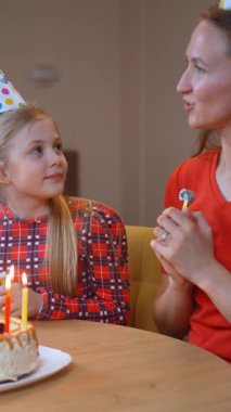 Mutlu bir aile doğum gününü kutluyor, anne gülümsüyor, pastada mumlar yanıyor, ve kızı heyecanla neler olduğunu izliyor, parti şapkaları takıyor ve masada oturuyor.
