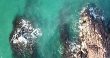 Dalgaların yukarıdan görünüşü mavi bir okyanusta kayalara çarpıyor. Deniz dalgaları güzel sahil manzaralı hava aracı 4K 'da. Kuş bakışı okyanus dalgalarının yukarıdan kayalıklara çarpması.. 