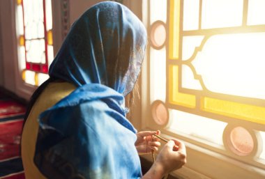 Başörtüsü ve başörtüsü takan Müslüman kadın, camide tespih tutarken elleri havada dua ediyor. Din dua kavramı.