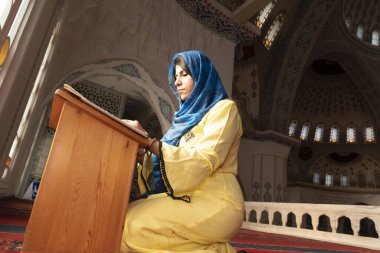 Başörtüsü ve tesettürlü Müslüman bir kadın camide Kuran okuyor. Din ve dua kavramı.