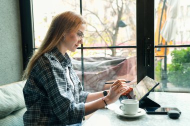 Ofis dışında üretken olmak. Çekici genç bir iş kadınının kafede otururken tabletinin üzerinde çalışmasının görüntüsü.. 