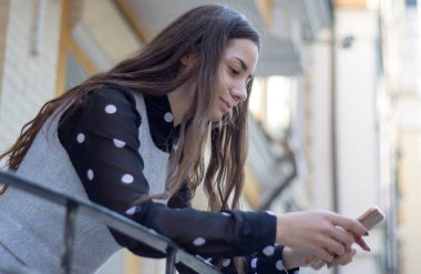 Çekici genç kadın okur veya metinler iletiye şehir evlerde karşı cep telefonu.