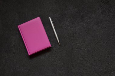Kalem ve defter ile Office Masaüstü. Siyah beton zemin üzerine Lila Not defteri. Soyut çimento arka planda vintage tarzı. Üstten görünüm.