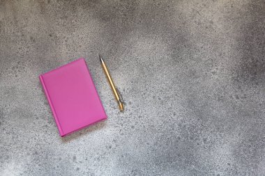 Pembe günlüğü bir gri beton zemin ve altın zarif tükenmez kalem. Office Masaüstü kalem ve pembe defter ile. Üstten görünüm.