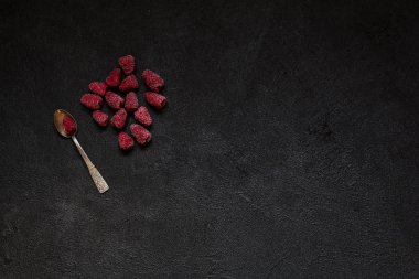 Gümüş kaşık siyah beton zemin üzerine ahududu meyveleri donmuş, metin veya yazıt için alan kopyalayın. Sağlıklı gıda fikir. Üstten görünüm.