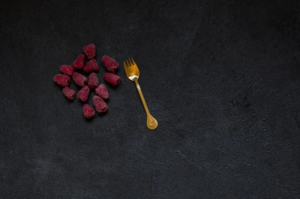 Dondurulmuş çilek, ahududu ve siyah bir taş zemin üzerine altın çatal. Sağlıklı gıda fikir. Üstten görünüm.