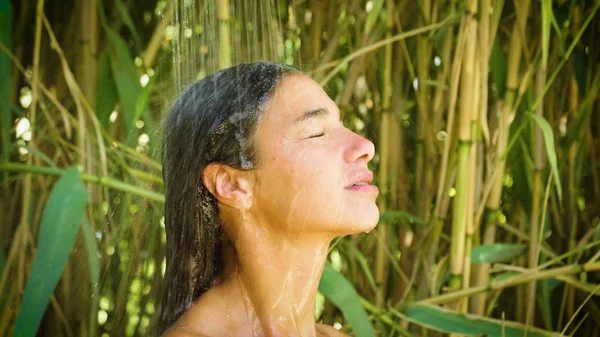 Beautiful young girl is washed in a tropical shower, happy, smiling, bamboo background. Concept: summer, heat, travel, vacation, day off, sun, freedom, refreshment, sexuality, enjoy, hot, holiday.