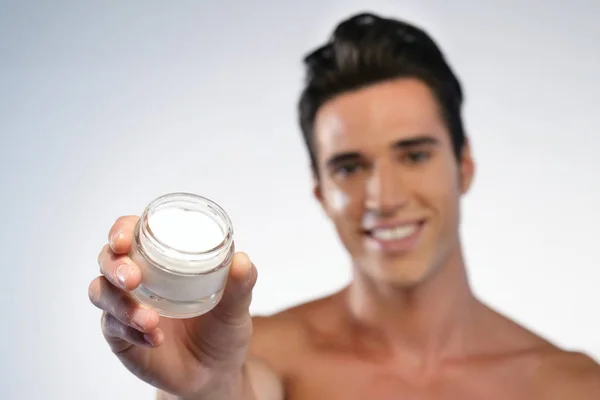 Close up of a man with moisturizer for his face smiling because he hydrates his skin and protects against impurities with anti-aging effects. Concept of: beauty and body care, creams, skincare