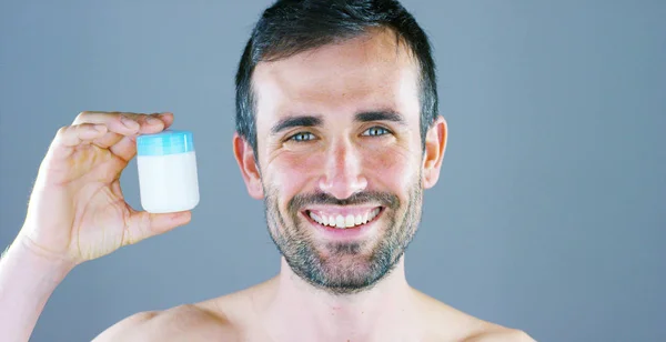 smiling happy caucasian man with stubble looking at camera and holding jar of cream