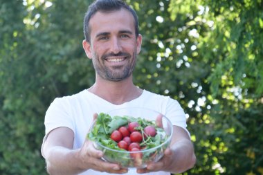 Açık havada yeşil ağaç yaprakları, taze salata cam kase ile ayakta ve kameraya bakarak adam