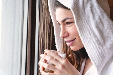 pencere beyaz bornoz giyiyor ve sıcak içecek bardağı tutan güzel kadın 